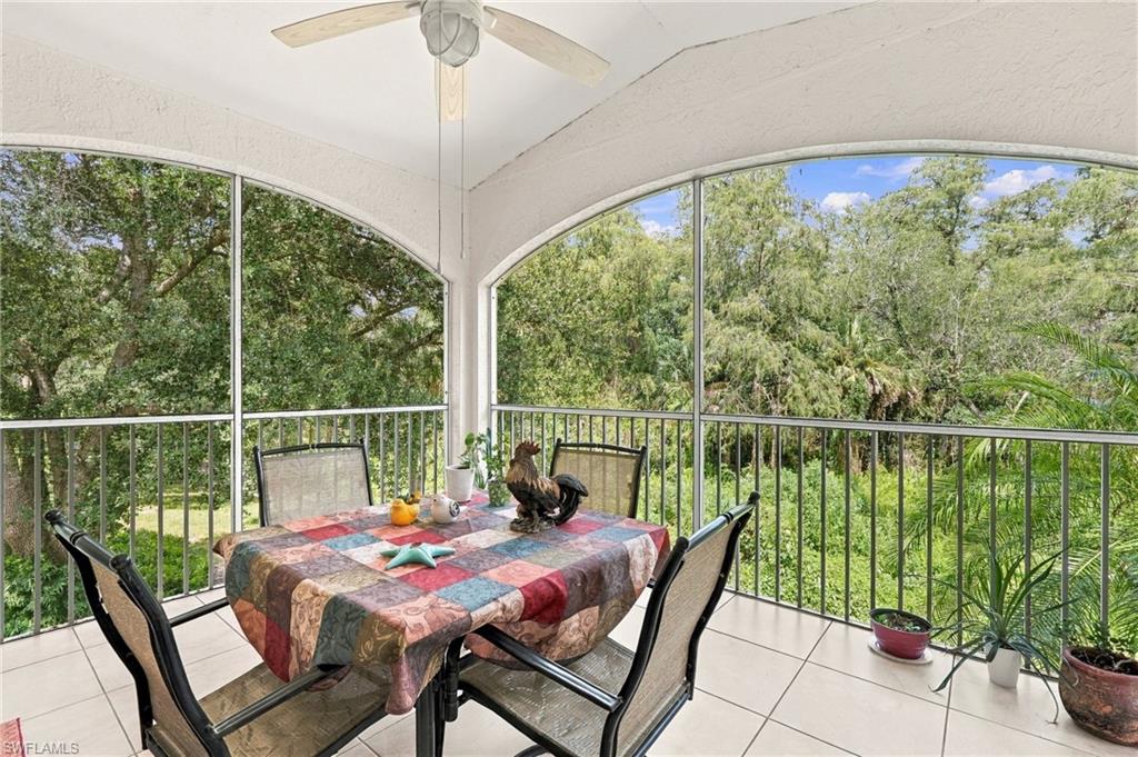 Screened lanai with a colorful dining table, arched enclosure, and leafy views.