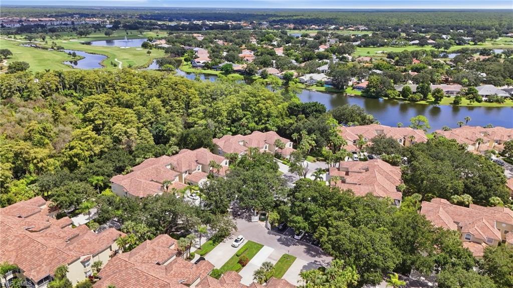 Aerial view of tiled-roof homes among trees beside a lake and golf course.