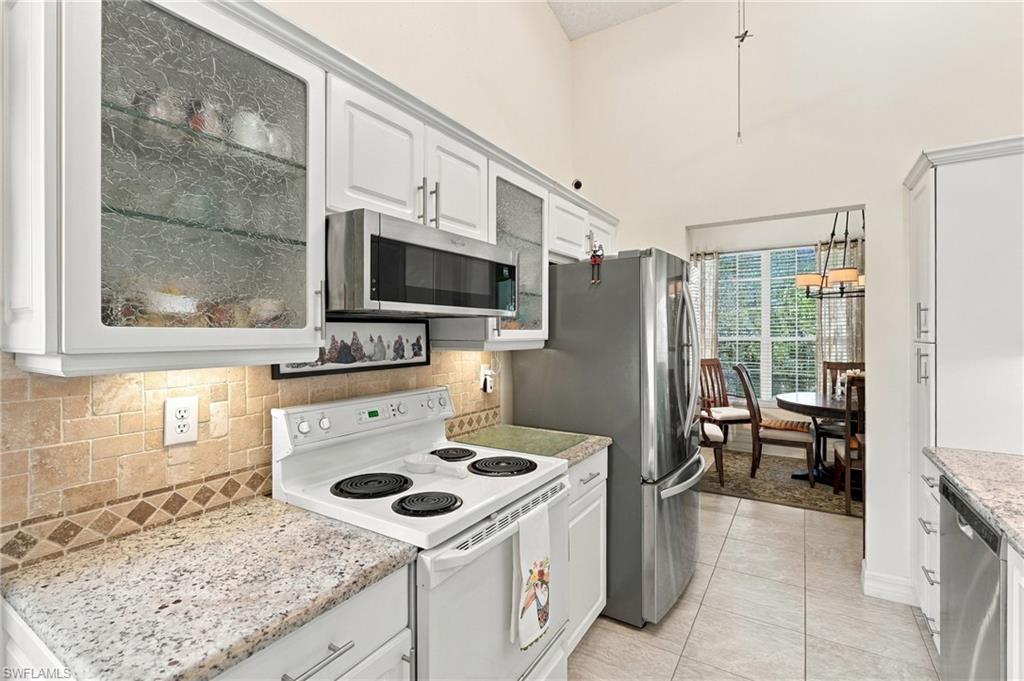 White kitchen with granite counters, stainless steel appliances, and a dining area by the windows.
