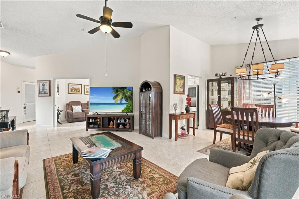 Open-plan living and dining room with gray sofas, tiled floors, and a beach scene on the television.
