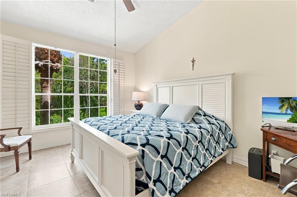 Furnished bedroom with a white paneled bed, patterned blue bedding, and a large shuttered window.