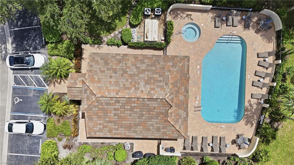 Aerial view of a home with a large pool, spa, tiled roof, and parking.