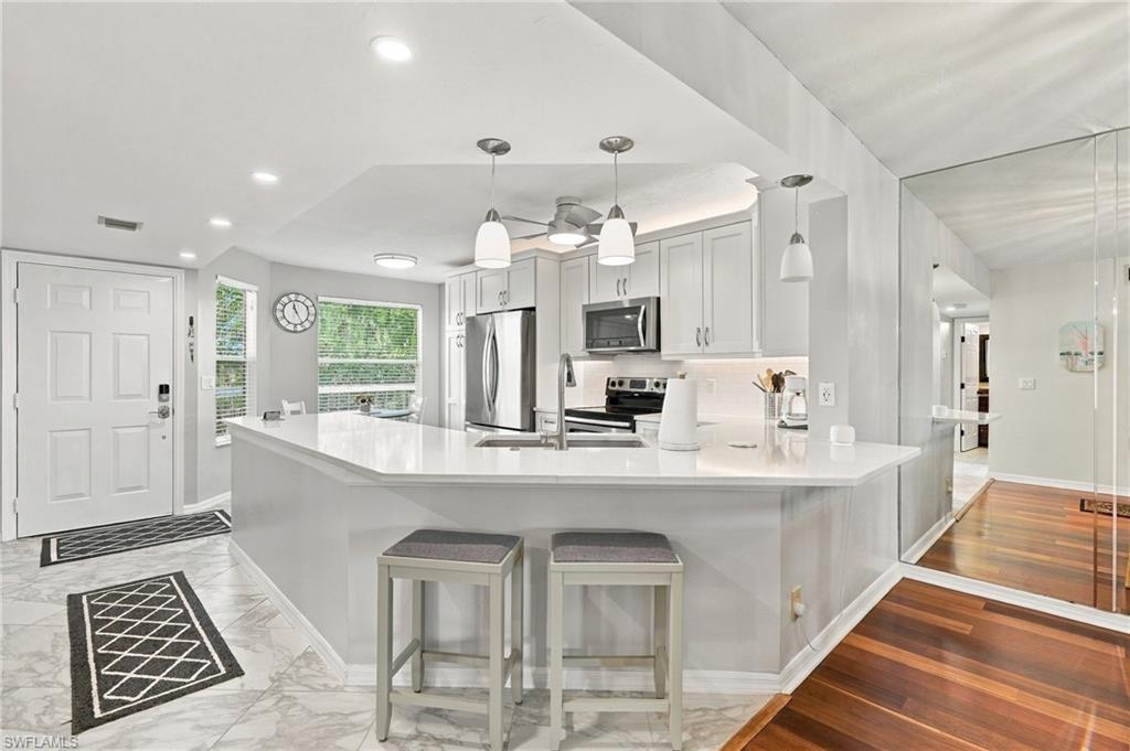 Bright kitchen with a large white island, stainless steel appliances, and marble-look tile flooring.