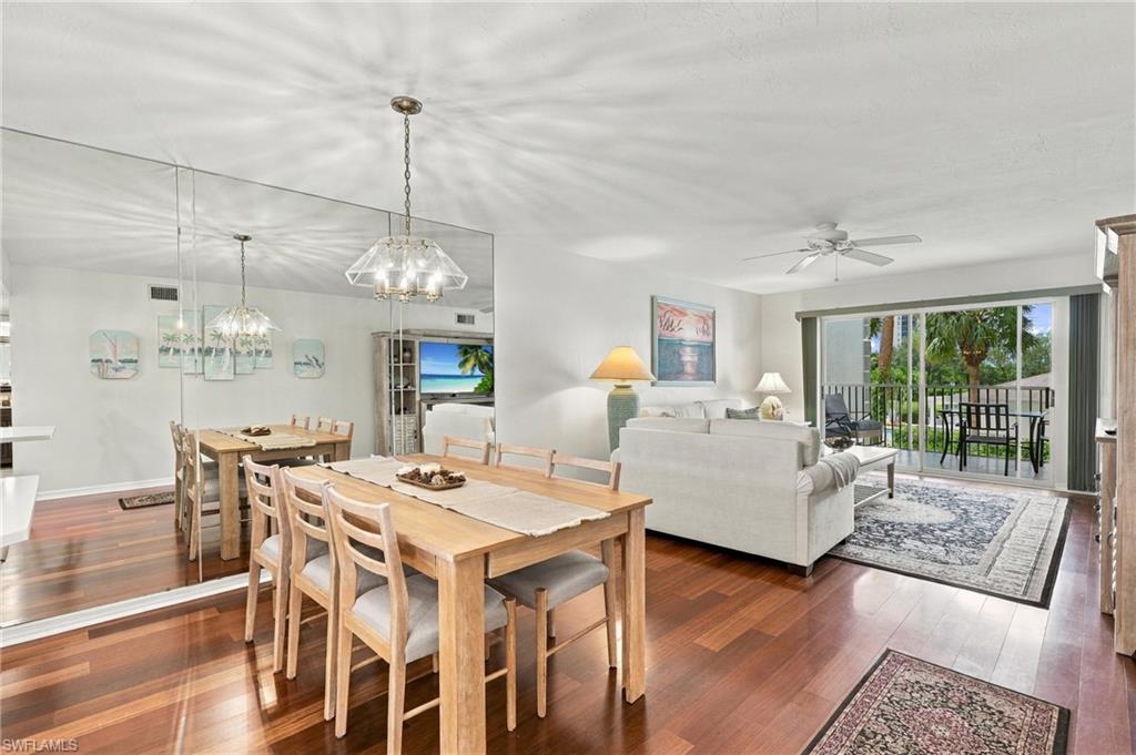 Open-plan dining and living room with a wooden table, white sofa, and balcony doors overlooking greenery.