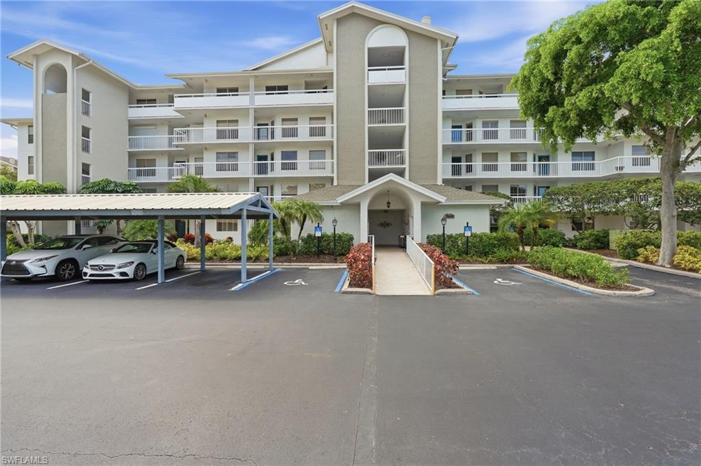 Multi-story condominium with white balconies, covered entrance, landscaped grounds, and carport parking.