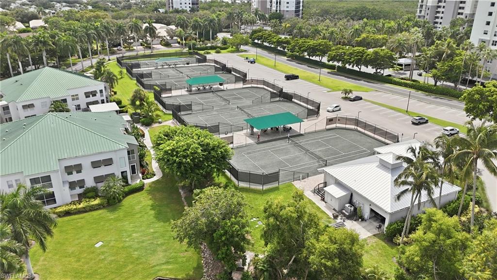 Aerial view of several fenced tennis courts with covered seating and palm trees.