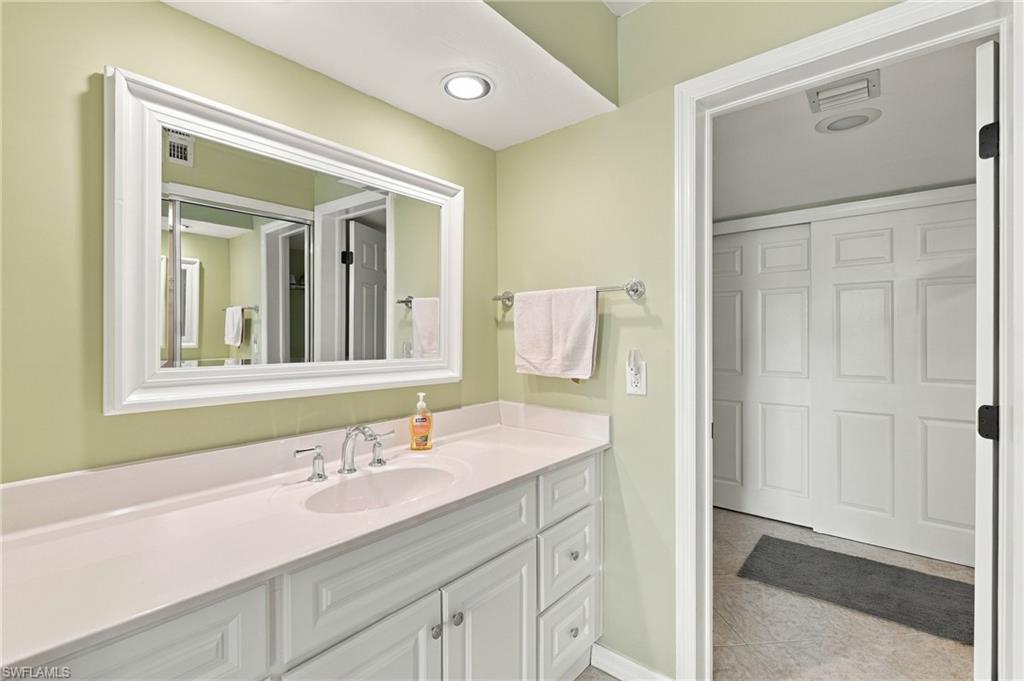 Bathroom vanity with white cabinetry, a large mirror, and an open doorway to a paneled-door closet.