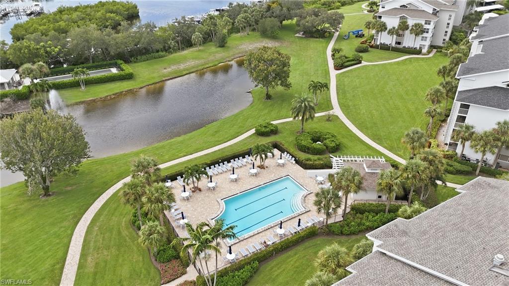 Aerial view of a community pool beside a pond, surrounded by landscaped grounds and condos.