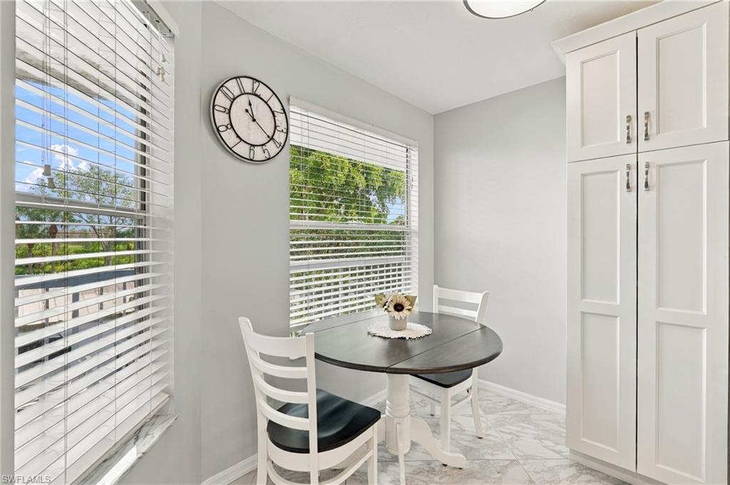 Breakfast nook with a round table, white chairs, built-in cabinets, and windows overlooking greenery.