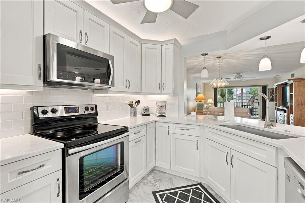 White kitchen with shaker cabinets, stainless steel appliances, and a large sink overlooking the living area.