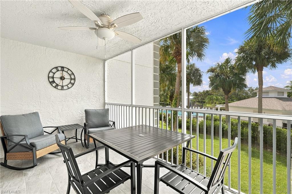 Furnished balcony with gray seating and dining set, overlooking palm trees and a glimpse of the pool.