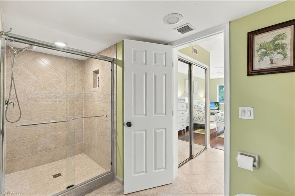 Bathroom with a glass-enclosed beige-tiled walk-in shower and doorway to a bedroom.