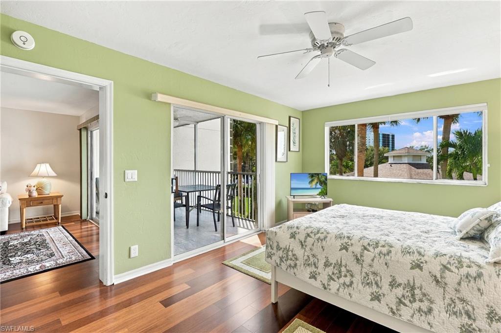 Bedroom with pale green walls, floral bedding, wood floors, and sliding doors to a screened balcony.