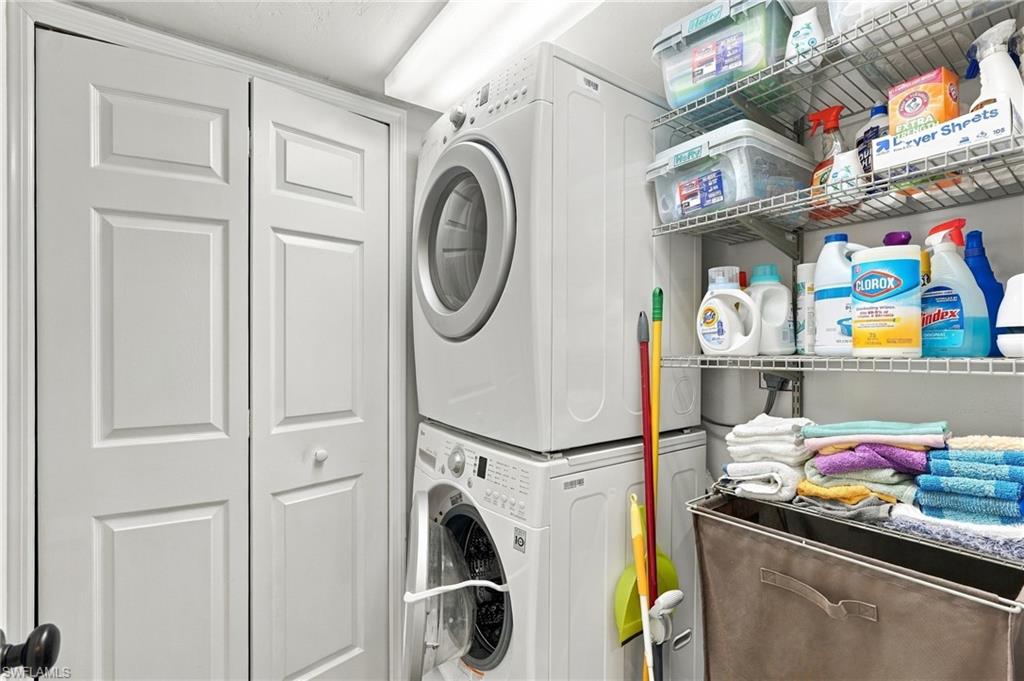 Laundry room with stacked front-loading washer and dryer, stocked wire shelves, folded towels, and a hamper.