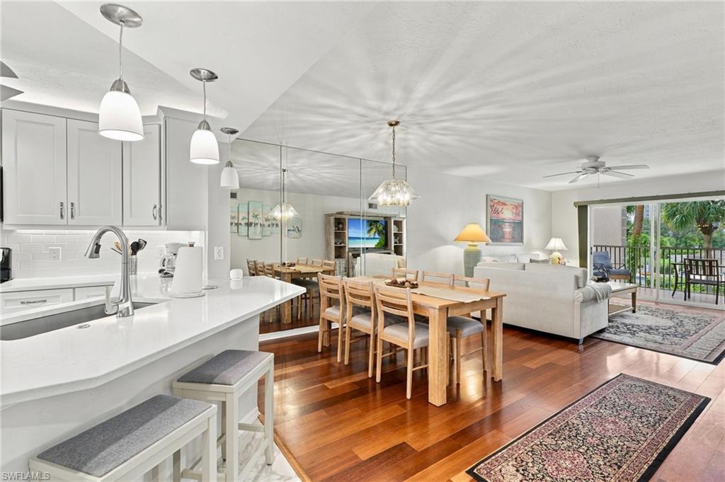 Open-plan kitchen, dining, and living area with white counters, hardwood floors, and sliding doors to a balcony.