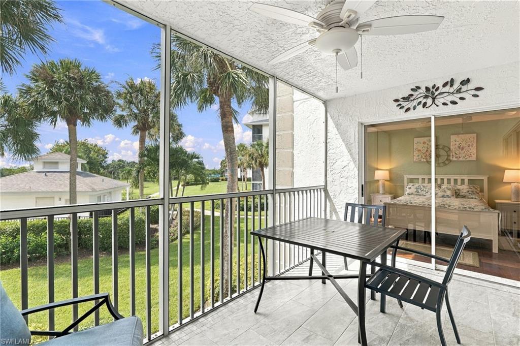 Covered tiled lanai with outdoor dining set, ceiling fan, palm trees, and lawn views.