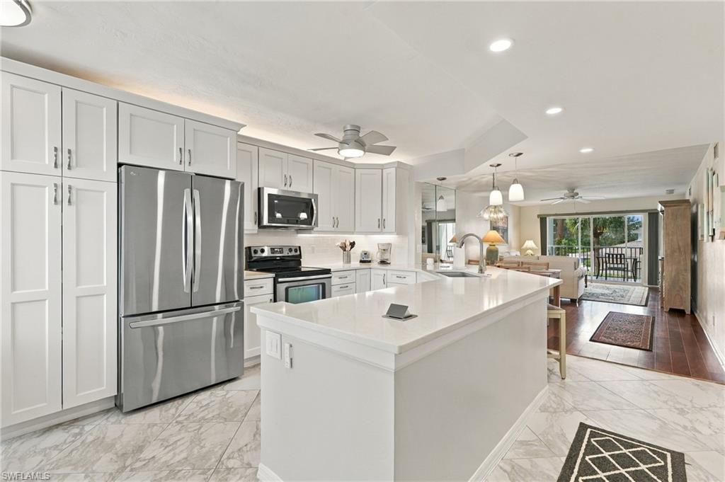Bright kitchen with white cabinets, a large island, stainless steel appliances, and an open view to the living area.