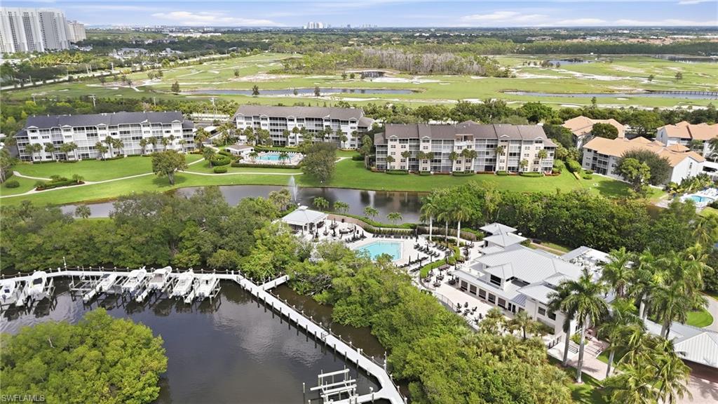 Aerial view of waterfront condos, pools, marina, and golf course greenery.