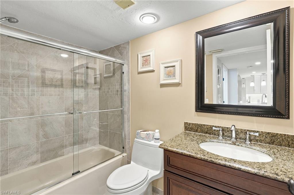 Bathroom with a glass-enclosed tiled tub, granite vanity, and dark wood cabinetry.