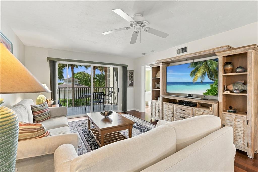 Living room with sectional sofas, built-in entertainment center, and sliding doors to a palm-lined balcony.