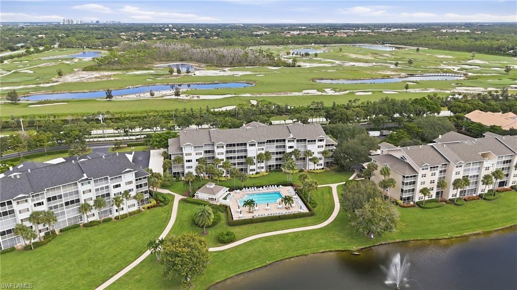 Aerial view of condominium buildings and a central pool beside a golf course and lake.