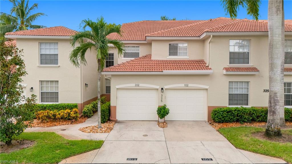 Two-story beige residence with a red tile roof, twin garages, palm trees, and landscaped grounds.
