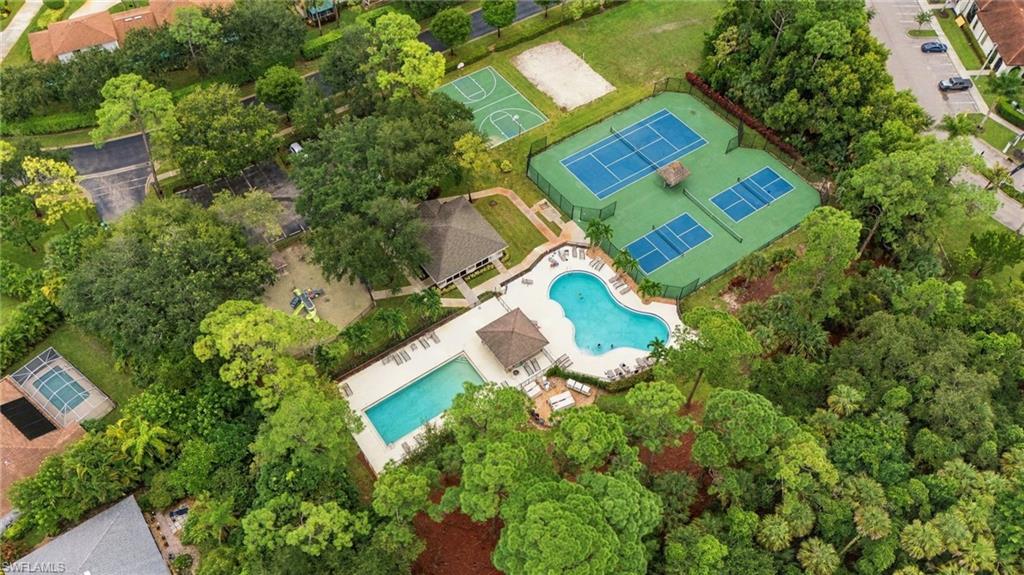 Aerial view of a residential community with two pools, tennis courts, and a basketball court.