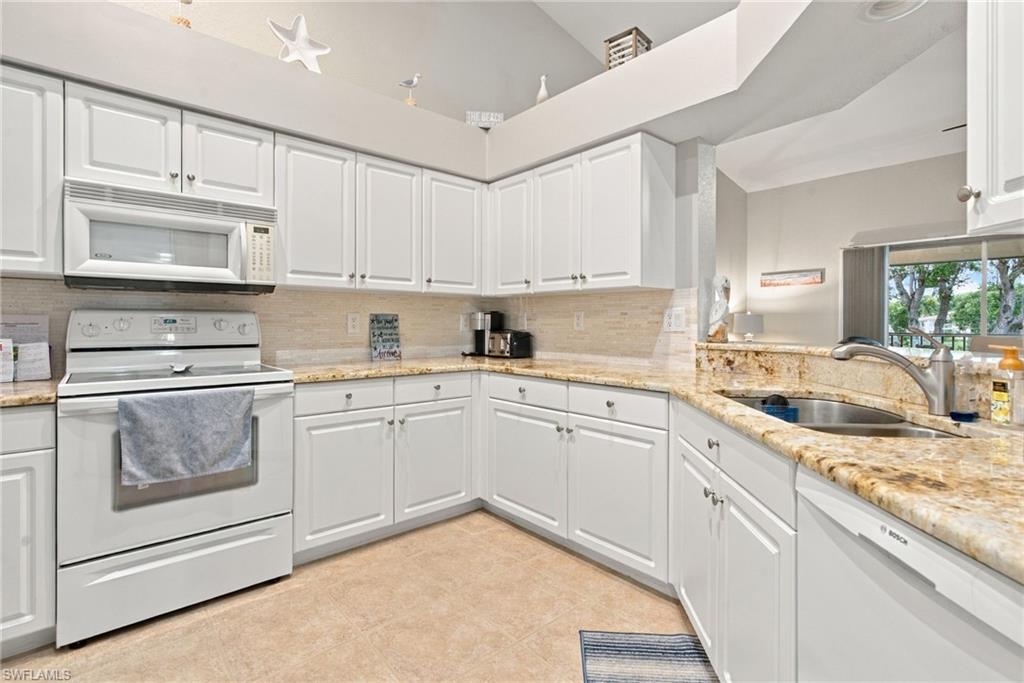 Kitchen with white cabinets, granite counters, and a sink overlooking a window.