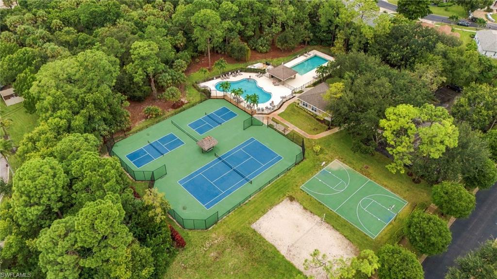 Aerial view of community tennis, swimming pools, and basketball court among trees.
