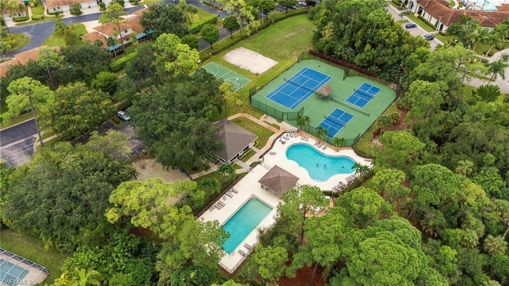Aerial view of community pools, tennis courts, and a pavilion among mature trees.