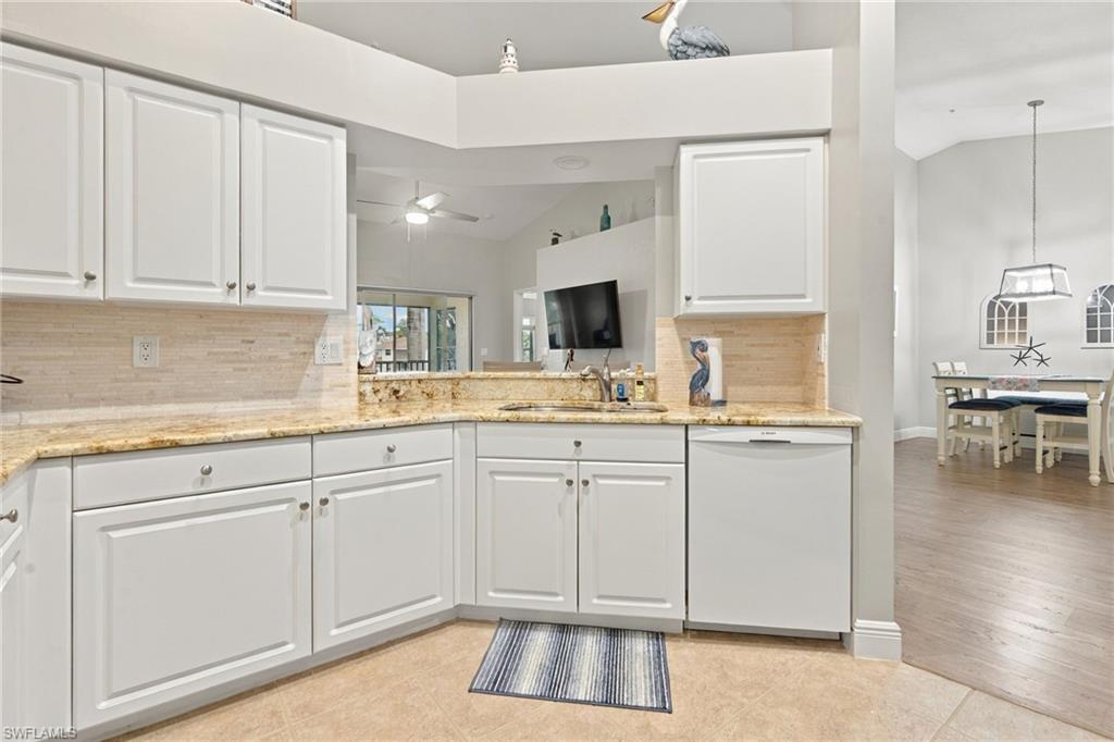 Condo kitchen with white cabinets, granite counters, and a dining area beyond.