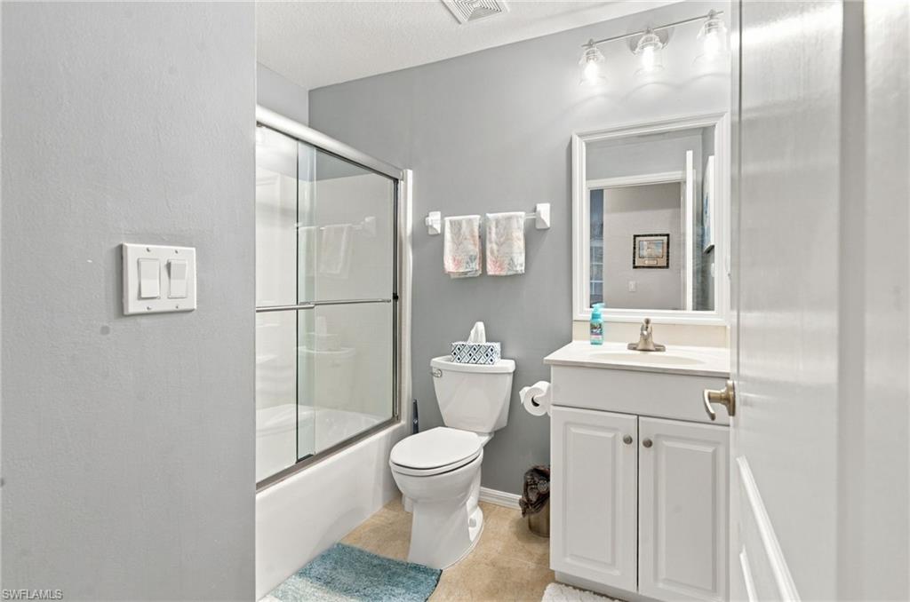 Bathroom with a glass-enclosed tub and shower, white vanity, and gray walls.