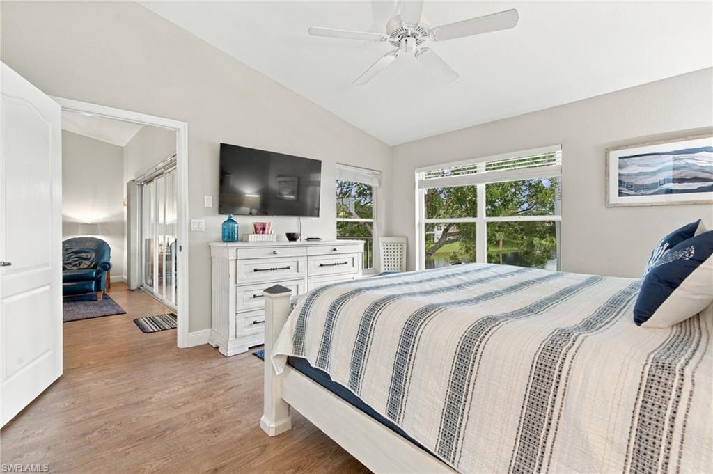 Bedroom with blue-striped bedding, a ceiling fan, and windows overlooking greenery.