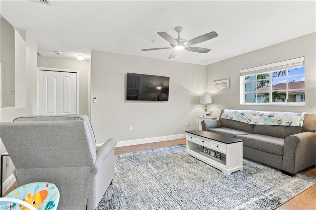 Living room with gray sofas, a wall-mounted TV, ceiling fan, and patterned area rug.