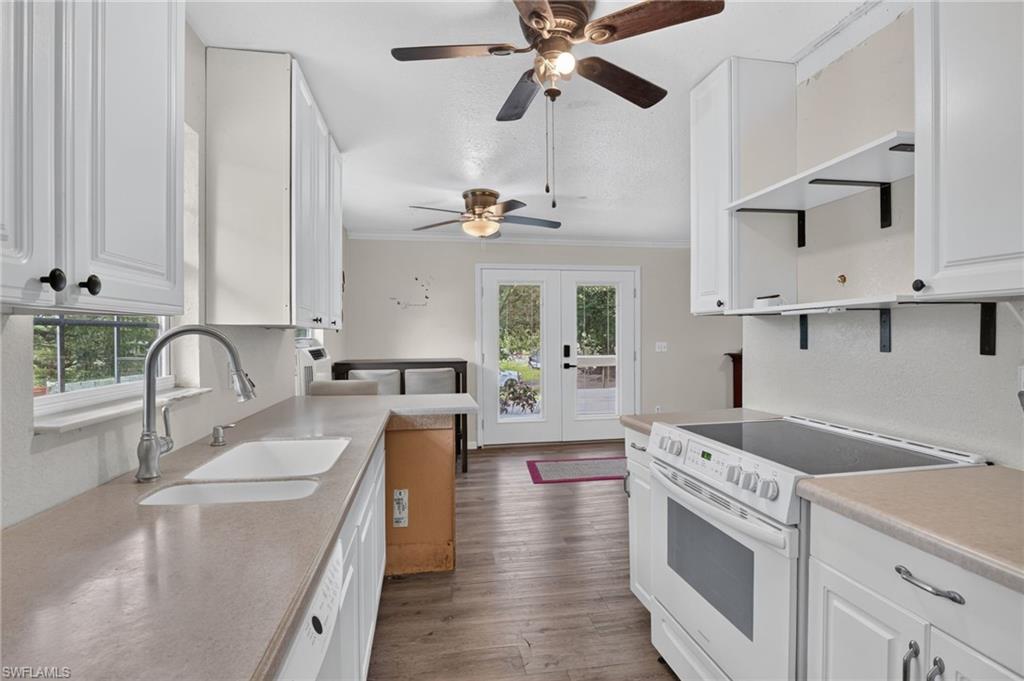 Kitchen with white cabinetry, a double-basin sink, electric range, and double doors opening outside.