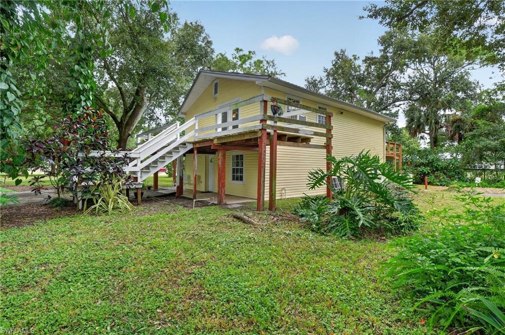 Raised yellow home with white exterior stairs and an upper deck amid mature trees.