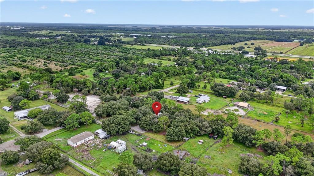 Aerial view of wooded rural acreage surrounded by homes, fields, and tree cover.