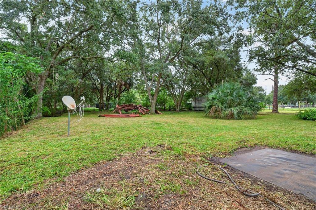 Grassy yard shaded by mature trees, with a satellite dish, lumber pile, and concrete pad.