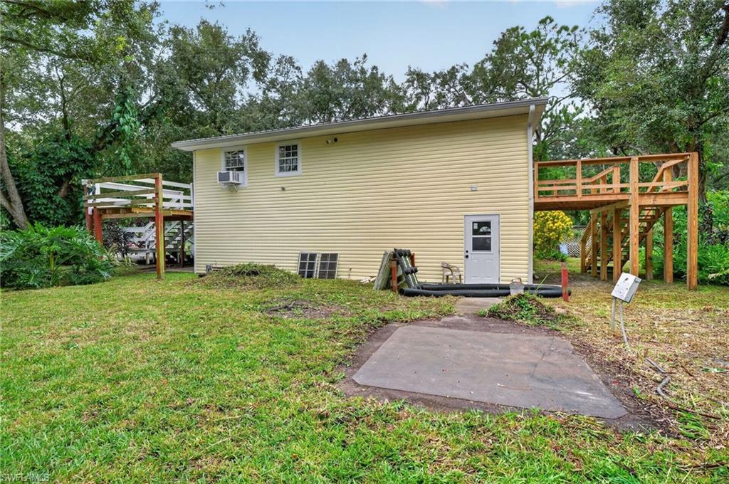 Rear of a yellow house with raised wooden decks on both sides and a concrete patio.