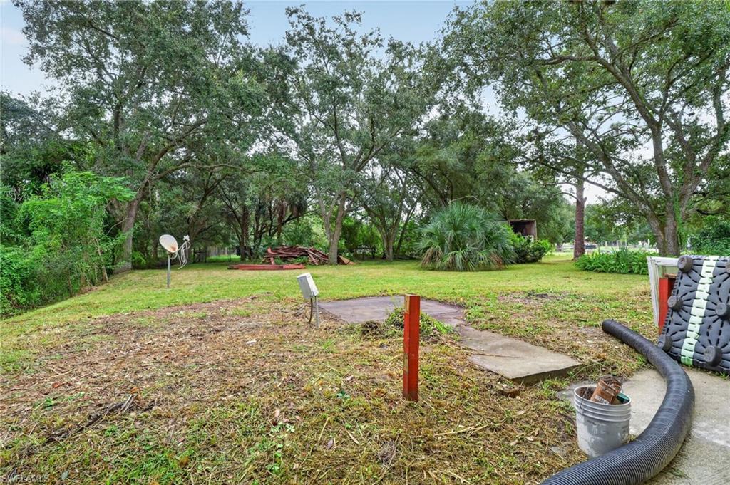 Tree-shaded grassy backyard with a concrete walkway, satellite dish, and stacked lumber.