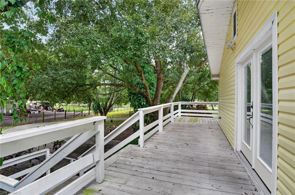 White-railed wooden deck beside a yellow-sided home, shaded by mature trees.