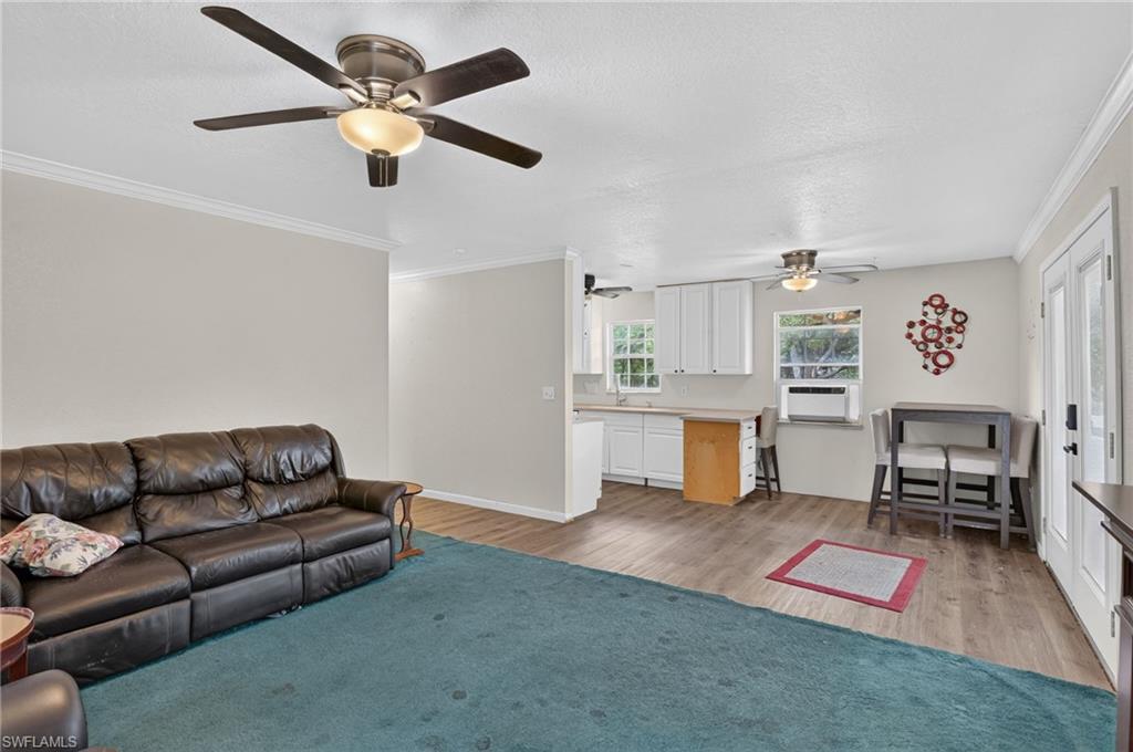 Living room with a leather sofa and teal rug, opening to a white kitchen and dining area.