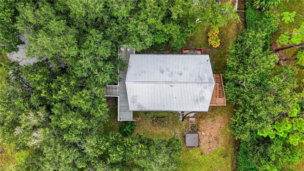 Aerial view of a metal-roofed house surrounded by dense trees, with decks and a small clearing.