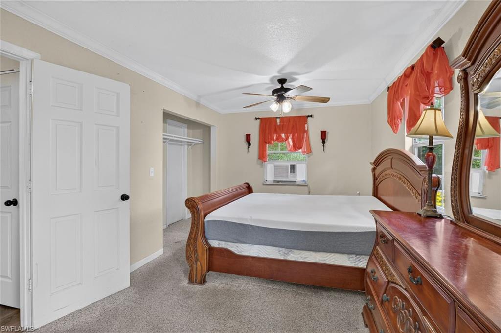 Bedroom with carved wooden bed, matching dresser, red curtains, and a window air conditioner.