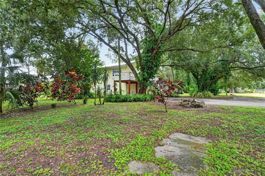 Two-story home beneath a broad oak canopy, surrounded by lush landscaping and mature trees.