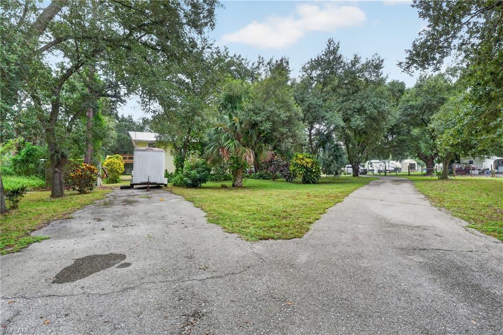 Wooded property with a forked paved driveway, mature trees, and trailers in the background.