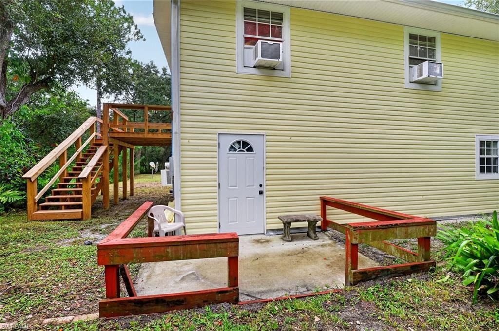 Yellow-sided two-story home with a raised wooden staircase and red railings around the entry pad.