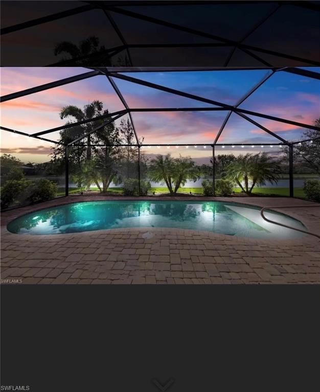 Screened pool and paver deck overlooking water beneath a pink and blue sunset sky.