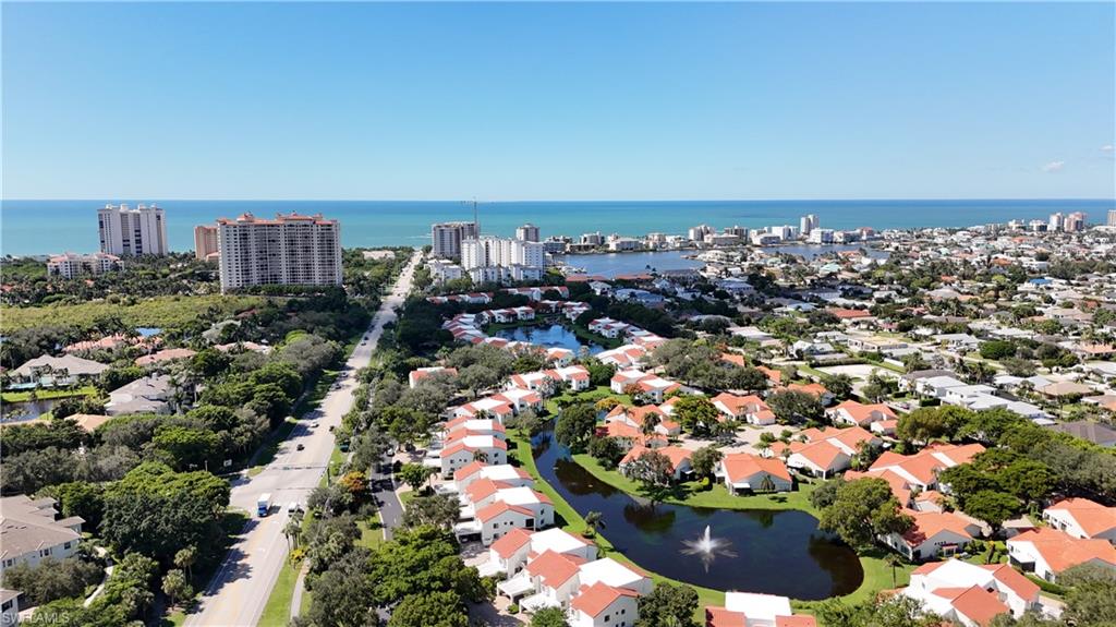 Aerial view of Naples homes around a pond, with the bay and Gulf in the distance.