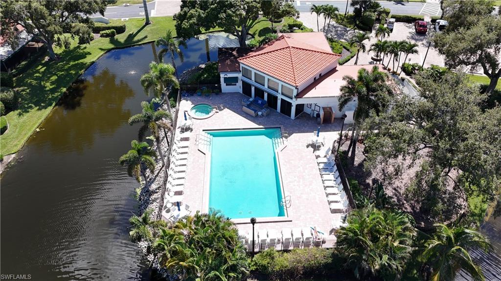 Aerial view of a tile-roofed building beside a pool and spa, surrounded by palms and a canal.